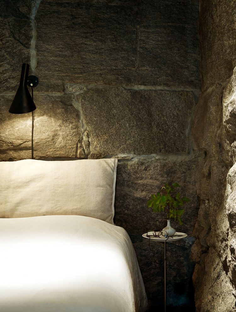 The rough stone walls here look somewhat cozy, which is unexpected, the secret is in soft textures of the bedding and a cute lamp.
