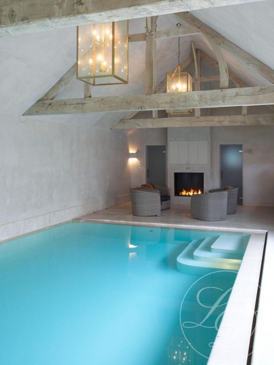 blue indoor pool with a poolside fireplace and chairs