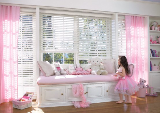 a pretty light pink and white girl's bedroom with light pink curtains and a windowsill upholstered bench, pink toys and books is pure cuteness