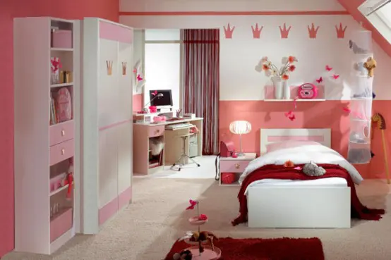 a lovely girl's bedroom with pink and white furniture, a peachy accent wall and burgundy rugs and textiles plus lots of toys