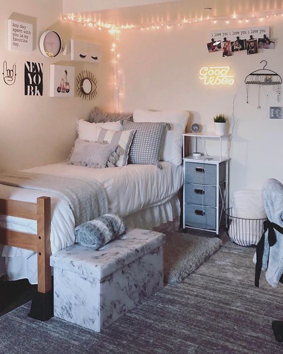 a neutral teen bedroom with a bed, a small storage nightstand, some lights and a pretty gallery wall plus a floral box for storage