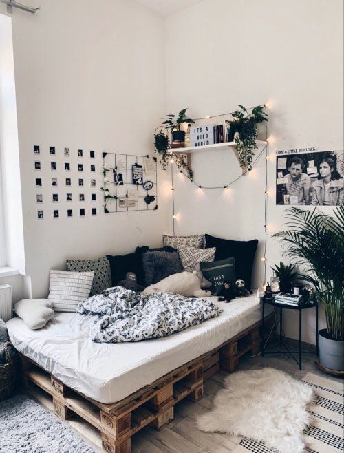 a simple and cool boho teen bedroom with a pallet bed, potted plants, a gallery wall and a grid, printed pillows and lights over the bed