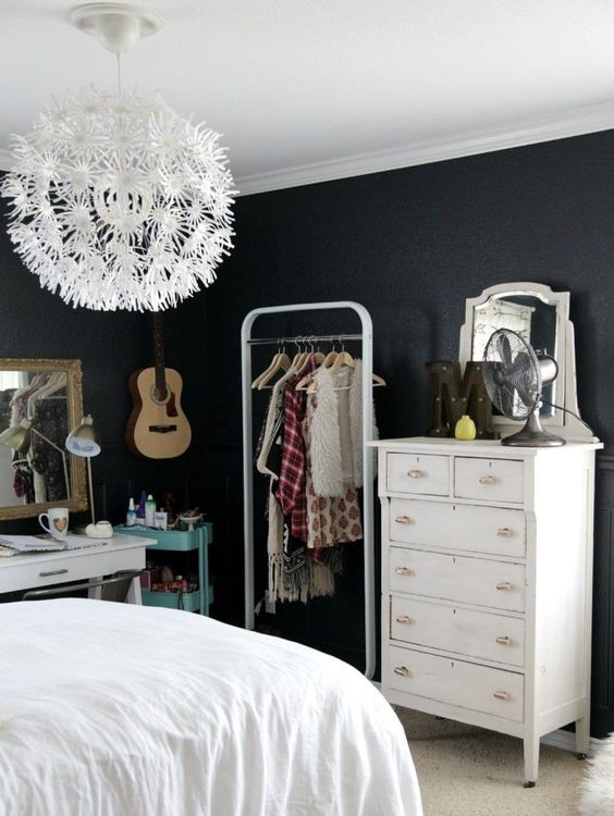 a stylish teen room with black walls, a dresser, a makeshift closet, a white desk, a turquoise storage cart and a floral chandelier