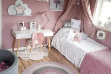 a dusty pink girl’s bedroom, with a bed with dusty pink bedding and a canopy, a striped rug, a gallery wall and some star-shaped pillows