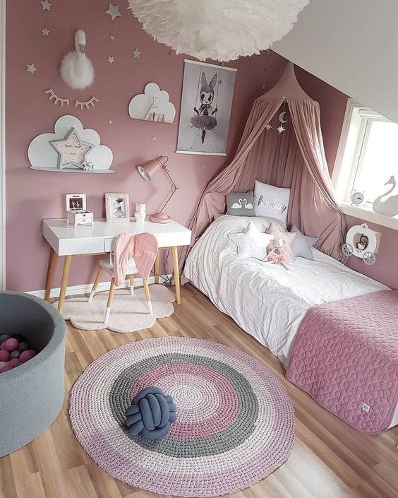 A dusty pink girl's bedroom, with a bed with dusty pink bedding and a canopy, a striped rug, a gallery wall and some star shaped pillows