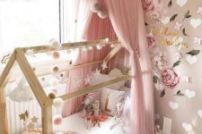 a gorgeous girl’s bedroom with tan and white walls with hearts and polka dots, a bed with a pink canopy, garlands and paitned blooms