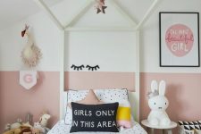 a modern girl’s bedroom with color block walls, a white cnaopy bed with polka dot bedding, side tables and a basket with toys