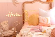 a pink and blush girl’s room with color block walls, a blush bed, blush bedding, mellow yellow pillows, a tassel chandelier and a wicker baby carriage