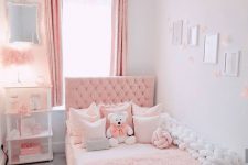 a pink and white girl’s room with a pink upholstered bed and a chest bench, a white shelving unit, fluffy pink lamps