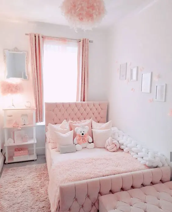 a pink and white girl's room with a pink upholstered bed and a chest bench, a white shelving unit, fluffy pink lamps