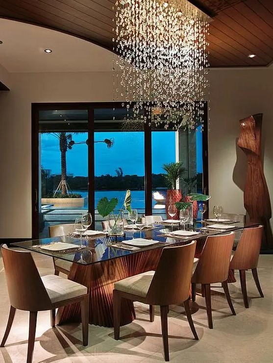 a sophisticated dining room with a glass top dining table and a bamboo base, chic upholstered chairs and a large bubble chandelier over the space