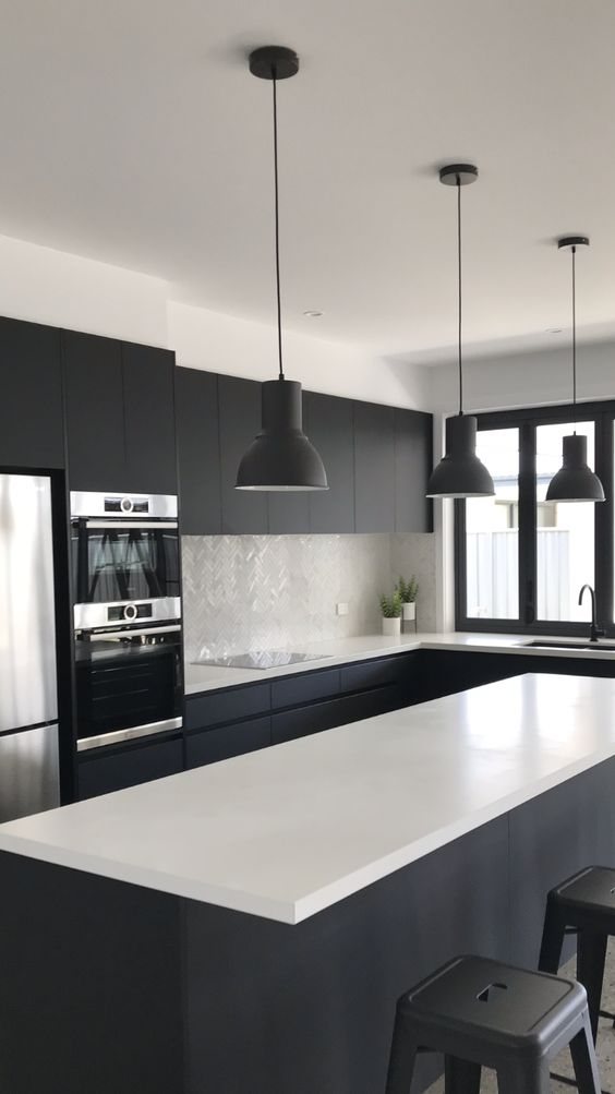 a bold black and white kitchen with matte cabinets, a large kitchen island, white coutnertops and a mother of pearl backsplash, black pendant lamps