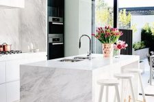 a chic white kitchen with white stone countertops and a backsplash and a waterfall coutnertop on the kitchen island