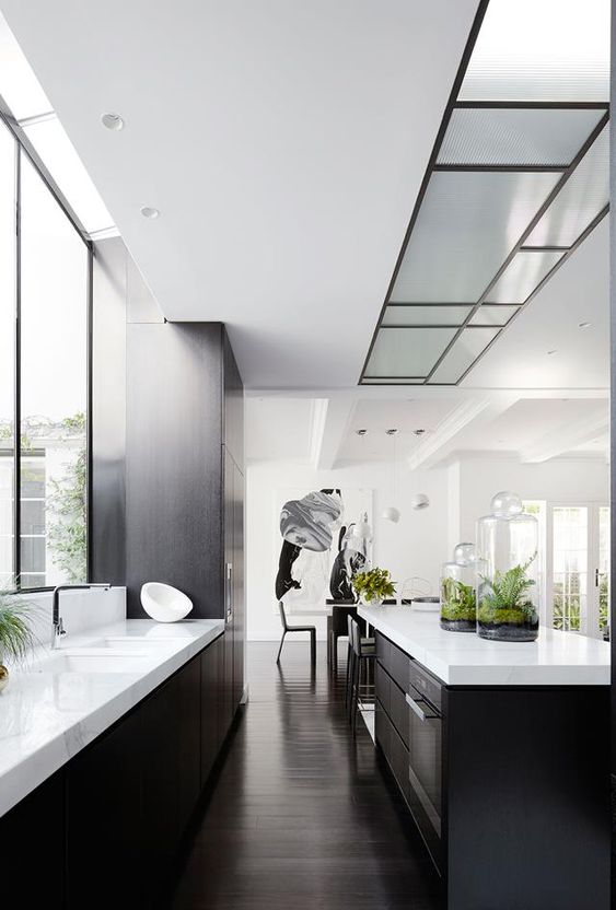 A contemporary black and white kitchen with white countertops, a window as a backsplash and built in lights