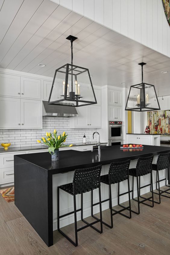 A mid century modern kitchen with white shaker cabinets, a white skinny tile backsplash, a black and white kitchen island and black woven stools