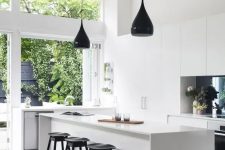 a miniamlist white kitchen with several black accents like a backsplash and pendant lamps, stools and fixtures looks airy and bright