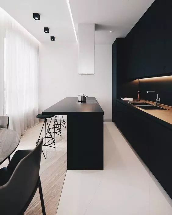 A minimalist black kitchen with built in lights, a matte kitchen island and a white hood is a stylish and chic idea to rock