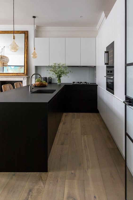 A minimalist kitchen with matte wihte and black cabinets, a large kitchen island, black built in appliances and pendant lamps