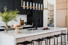 a refined modern kitchen with matte black cabinets, a white kitchen island with a white stone countertop, a chic chandelier and black fixtures