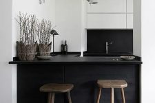 a small minimal black and white kitchen with a kitchen island and dining space in one, with mismatching wooden stools and a white lamp