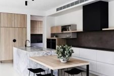 a stylish contemporary kitchen with white lower cabinets, open storage shelves, a black hood, black countertops, light stained wood and a stone kitchen island