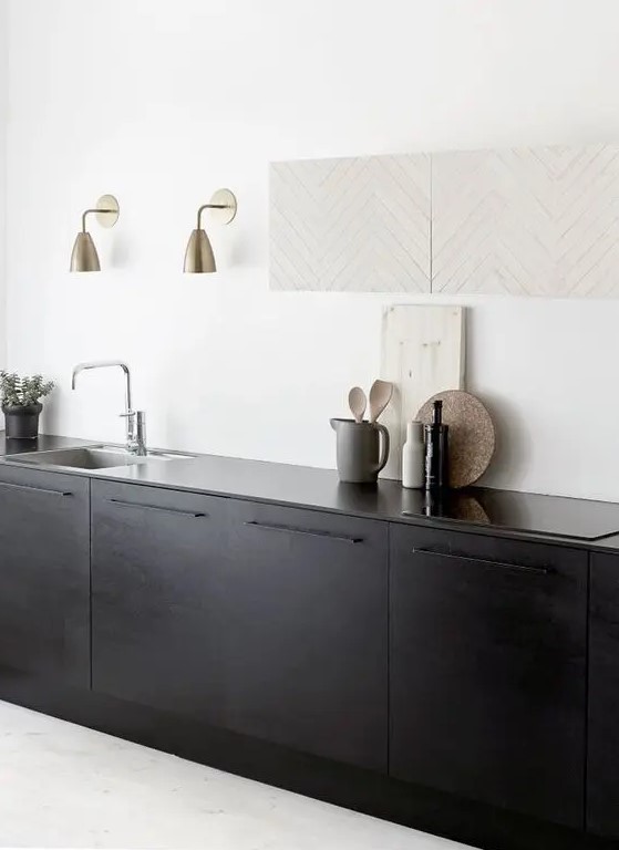 a subtle kitchen in white, with matte black cabinets and black countertops, gold sconces is a lovely and airy contemporary space