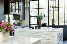 an elegant vintage kitchen with black cabinets and two white kitchen islands, cage-like pendant lamps and a large window to enjoy the view of the garden