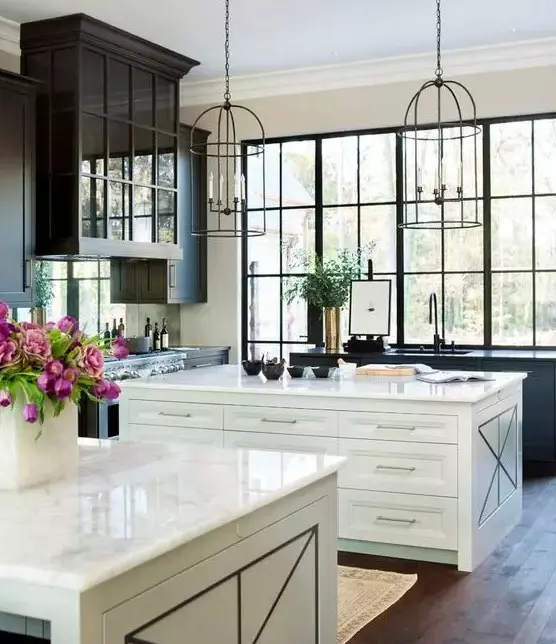 An elegant vintage kitchen with black cabinets and two white kitchen islands, cage like pendant lamps and a large window to enjoy the view of the garden