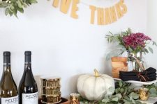 a Thanksgiving food and drink station with a plaid runner, a white pumpkin, pink florals and wreaths over it
