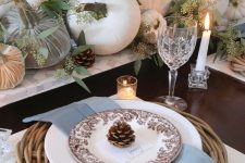 a Thanksgiving table with velvet and natural pumpkins, greenery, pinecones, a woven charger and blue napkins