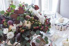 a beautiful Thanksgiving centerpiece of greenery, dark foliage, berries, white blooms and some fresh fruits