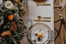 a beautiful Thanksgiving tablescape with striped napkins, gold cutlery, a greenery runner, blooms, citrus and candles