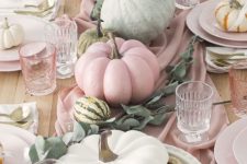 a beautiful pastel Thanksgiving tablescape with a blush runner, plates and glasses, some natural pumpkins and greenery