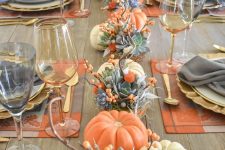 a bright modern Thanksgiving table with pumpkins, succulents, berries and orange placemats and grey napkins and gold glasses