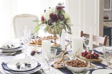 a chic Thanksgiving table setting with a printed table runner, blue napkins, a bold floral arrangement and candles