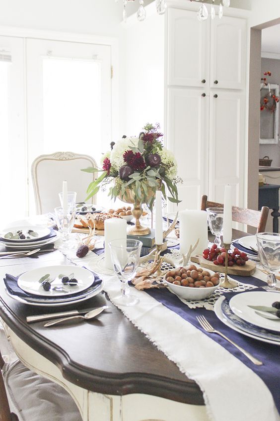 a chic Thanksgiving table setting with a printed table runner, blue napkins, a bold floral arrangement and candles