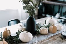a modern Thanksgiving table with white pumpkins – real and cardboard ones, a greenery arrangement in a black vase and black plates