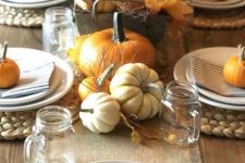 a pretty rustic Thanksgiving table with striped napkins, a burlap runner, orange and white pumpkins, jar mugs and leaves