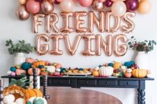 bright Thanksgiving decor with bold pumpkins of various sizes, greenery, bold ballons and balloon letters over the table