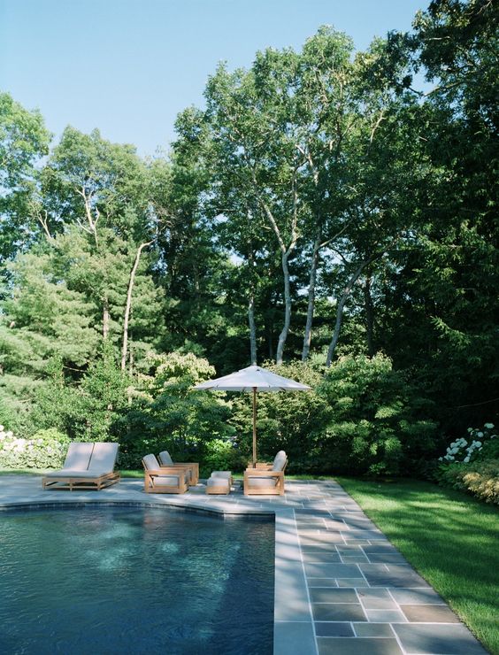 a stylish modern outdoor space with a catchily shaped pool, a stone deck, neutral seating furniture and a parasol