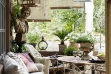 a Provence-inspired outdoor living room with rattan and metal furniture, neutral and pastel textiles, potted greenery and blooms and some pendant lamps