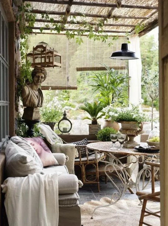 A Provence inspired outdoor living room with rattan and metal furniture, neutral and pastel textiles, potted greenery and blooms and some pendant lamps