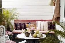 a boho outdoor living room with colorful textiles and rugs, potted greenery and a white wicker chair