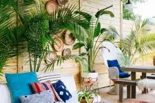 a boho outdoor living room with potted plants, a white sofa, boho rugs and an ottoman, a living edge table and decorative baskets on the wall