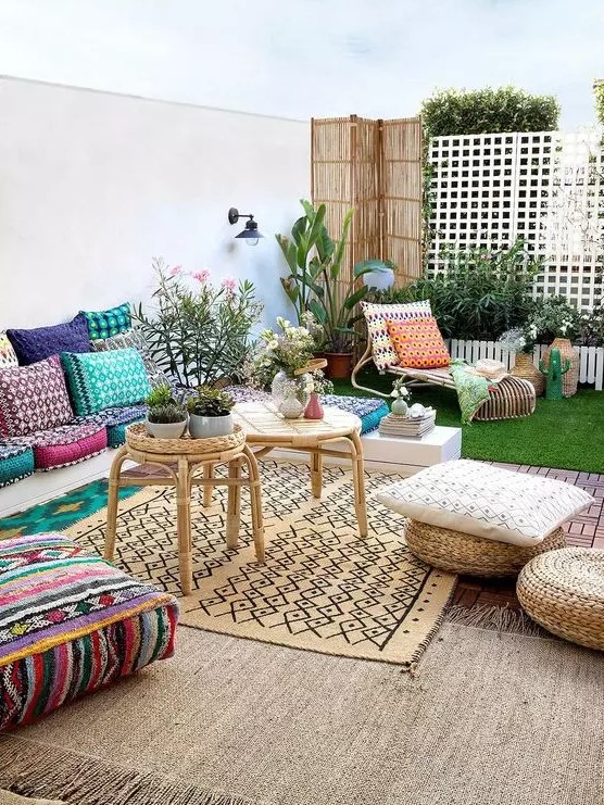a bold boho outdoor living room with super colorufl pillows and cushions, layered rugs, rattan coffee tables and potted plants