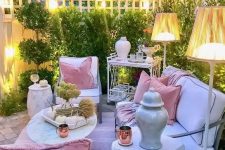 a chic pastel outdoor living room with white contemporary furniture, floor lamps, refined tables and a greenery wall