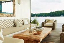 a coastal rustic outdoor living room done in neutrals with a corner sofa with tan upholstery, a stained coffee table, wicker chairs and a lage mirror in a driftwood frame