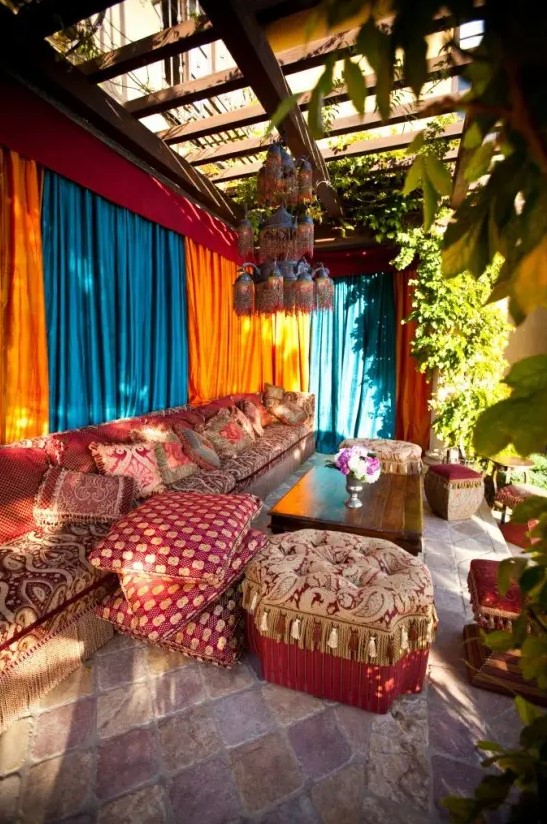 A colorful Morocco style outdoor living room with turquoise and orange curtains, soft seating furniture with bright upholstery, potted greenery