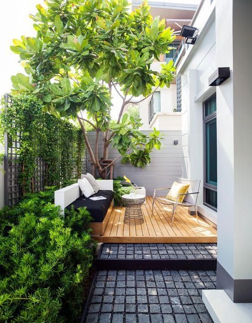 A contemporary outdoor space with a built in bench in black and white, a deck, a comfy chair and a coffee table