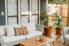 a cool modern outdoor living room with neutral woven furniture, printed pillows, a wooden table and potted plants welcomes